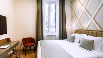 Una habitación de hotel con una cama, un escritorio, una silla y un ventanal con cortinas.