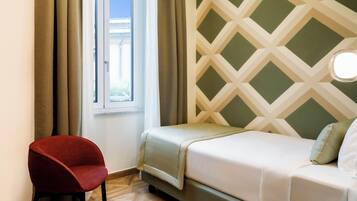 A room with a bed, a red chair, a window with curtains, and a patterned wall.