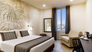 Une chambre d’hôtel avec un grand lit, un canapé, une table à manger avec des chaises et une vue sur les immeubles par la fenêtre.