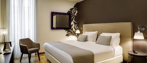 A hotel room with a large bed, a chair, a desk with a lamp, and a wall-mounted mirror.