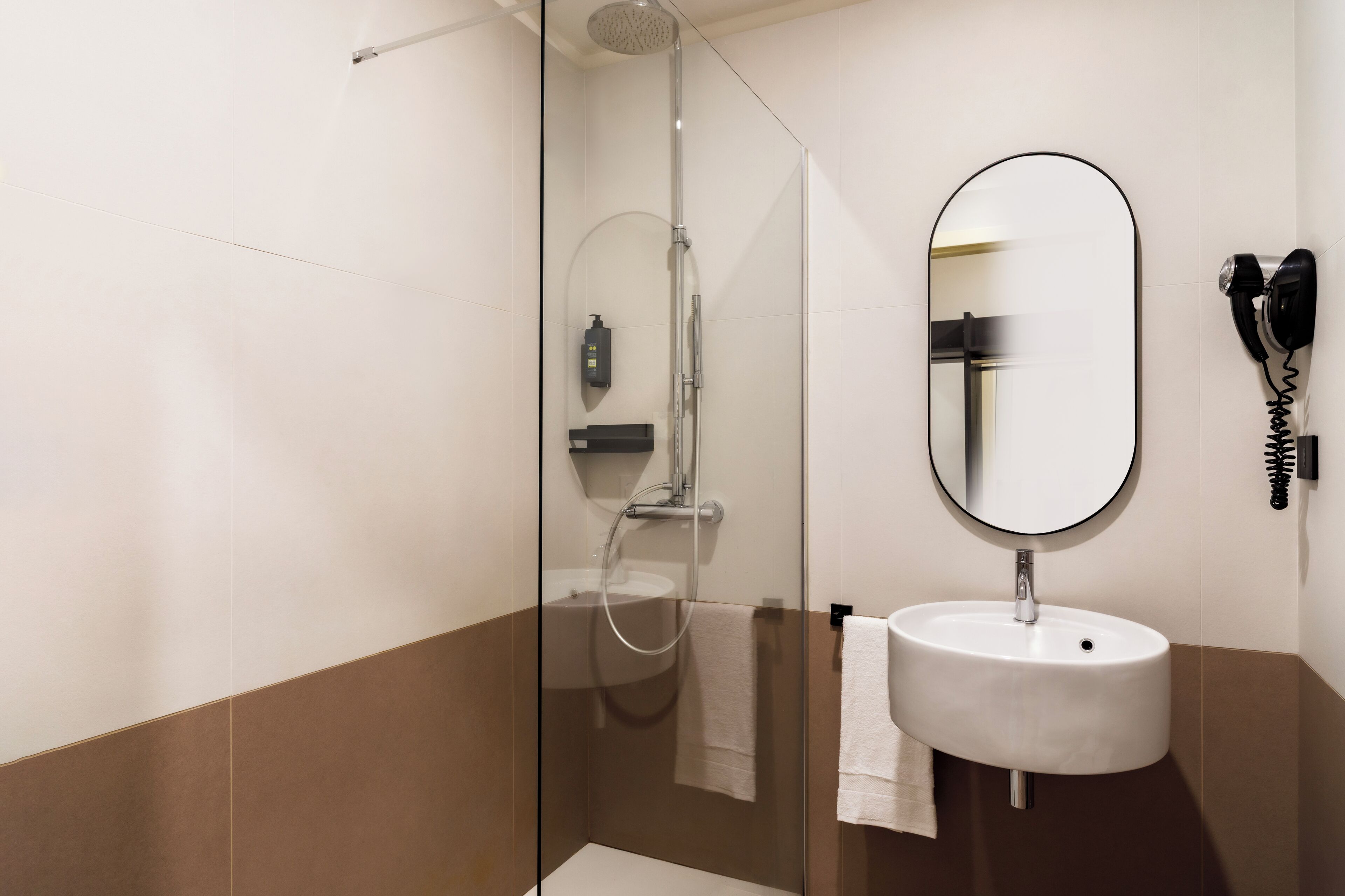 Ein modernes Badezimmer mit einer in Glas eingefassten Dusche, einem runden Spiegel und einem weißen Waschbecken.