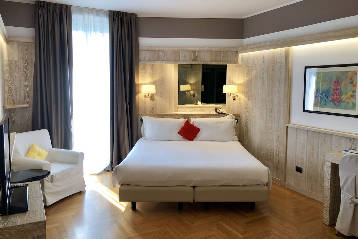 Una habitación de hotel con una cama grande, una mesita de noche, una silla, un escritorio y un espejo.