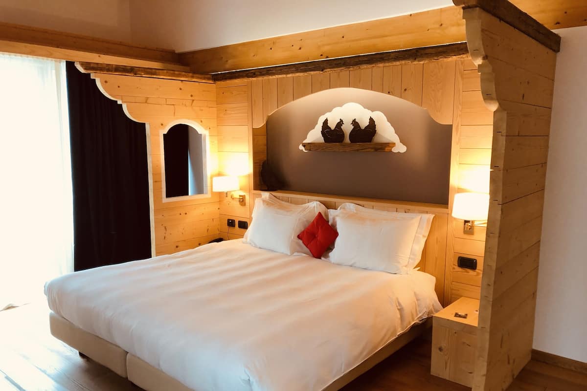 Un dormitorio con estructura de madera, una cama, dos lámparas de noche, una mesita de noche y un estante decorativo con dos figuritas.
