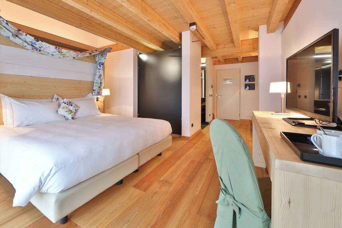 Un dormitorio moderno con techo de madera, una cama con ropa blanca, un escritorio con computadora y un televisor.