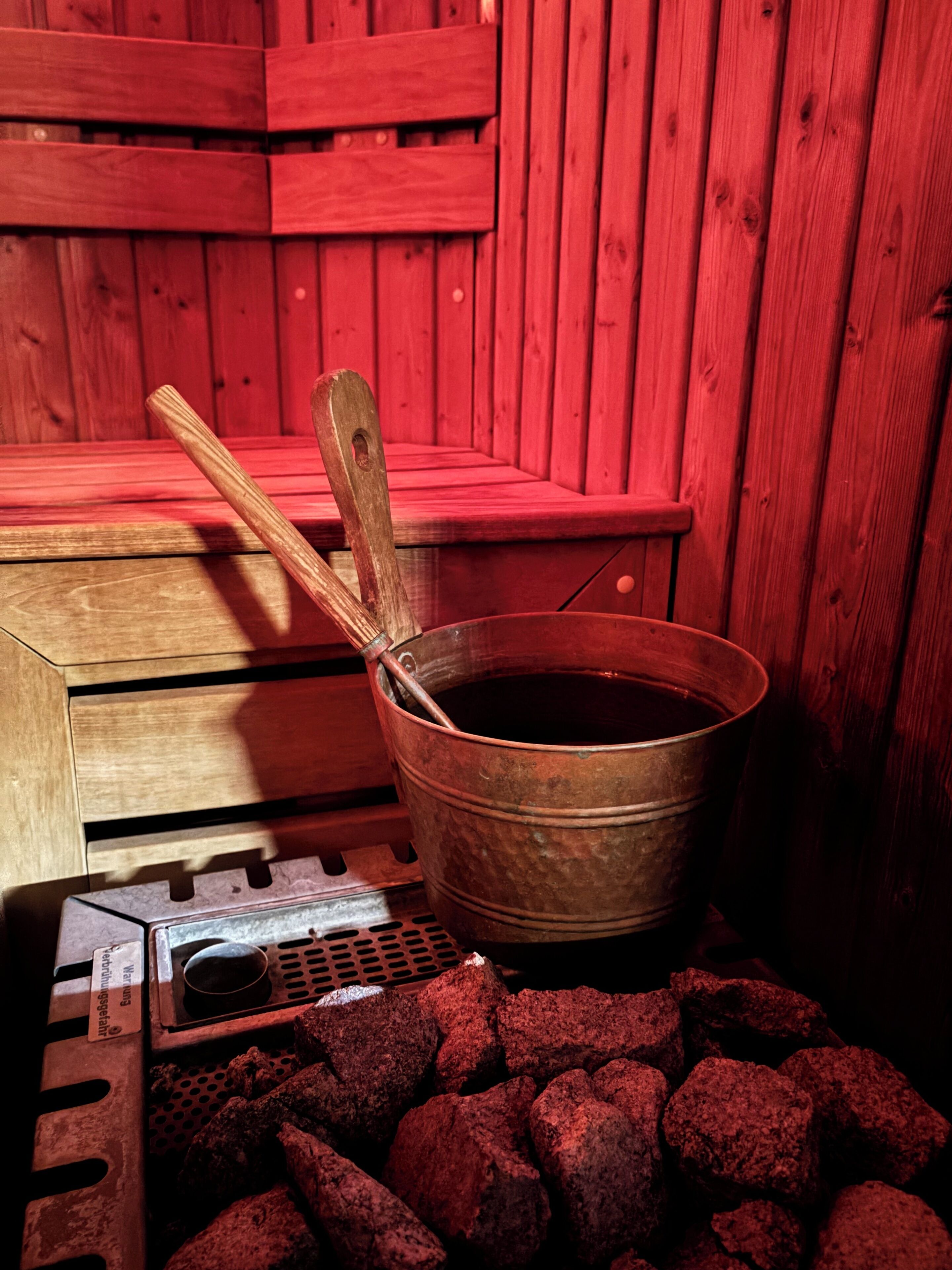 Una sauna con banco de madera, un cubo metálico y un calentador.