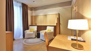 Habitación de hotel con dos sillones blancos, un escritorio de madera, una lámpara, un tapete redondo y un armario.