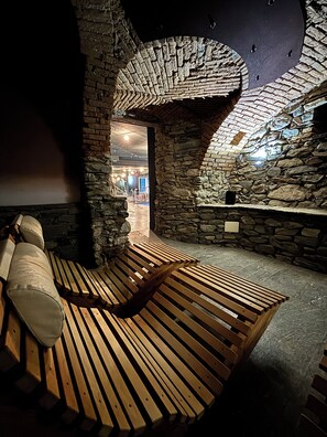A stone-walled room with a wooden bench and a small table. - Hotel Alla Posta (Saint-Vincent)