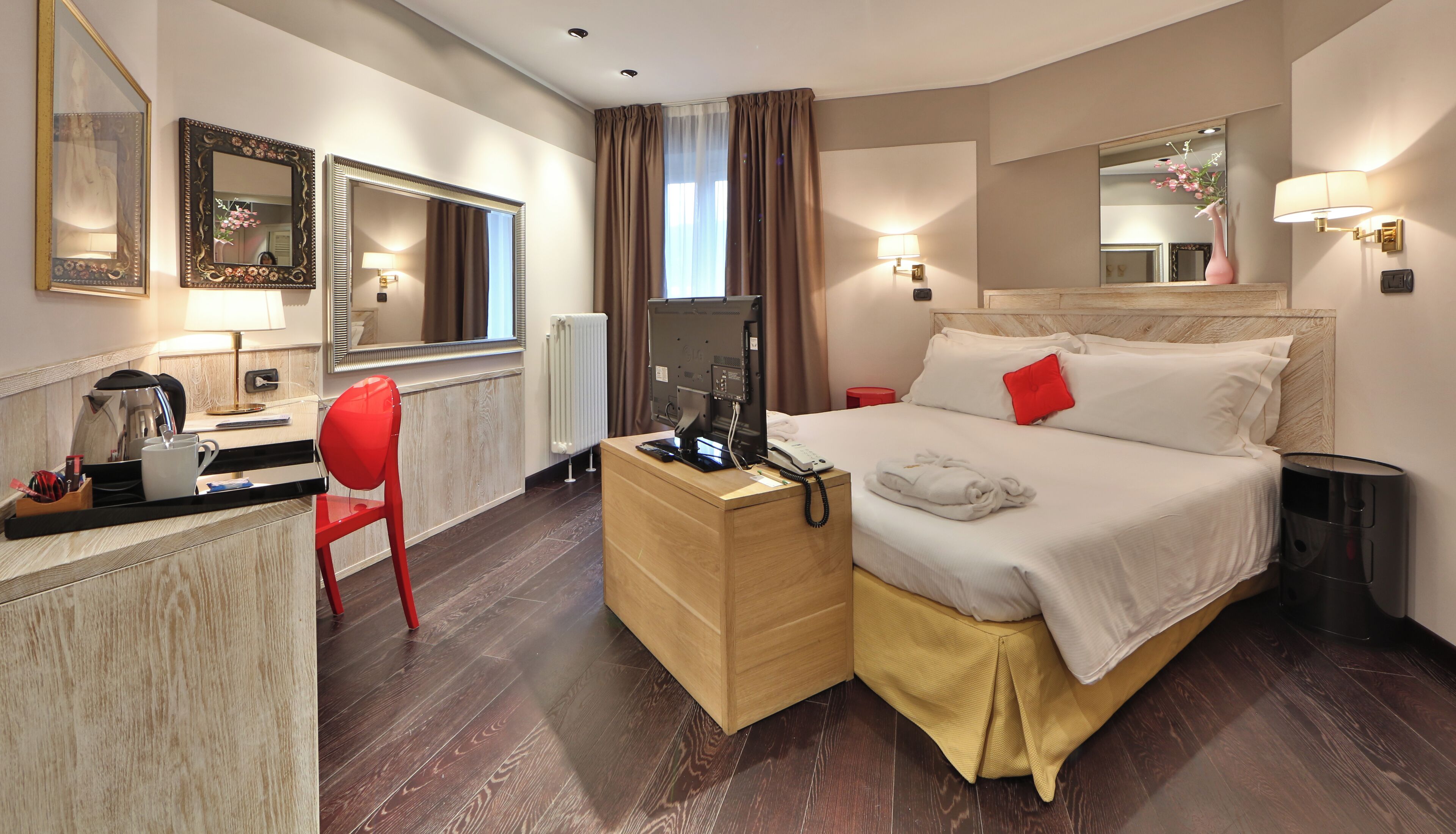 Une chambre d’hôtel comprenant un lit, une table de chevet, une télévision, un bureau avec une chaise et un miroir.