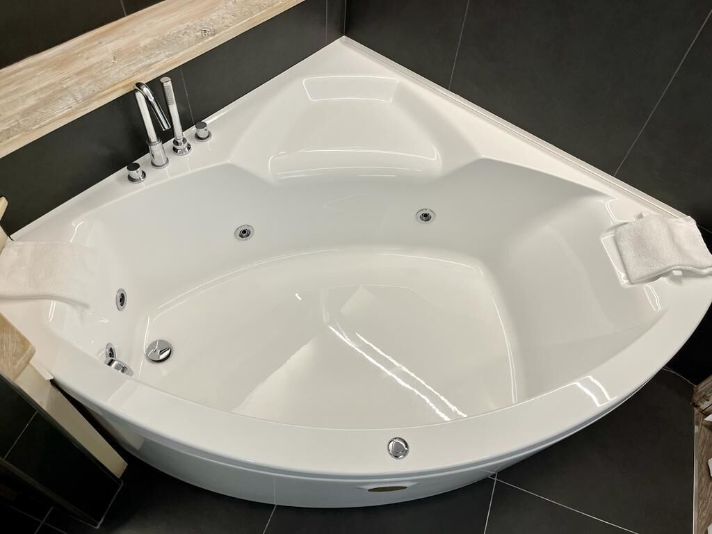 A modern bathroom with a freestanding bathtub, a wooden vanity, and dark tiled walls.