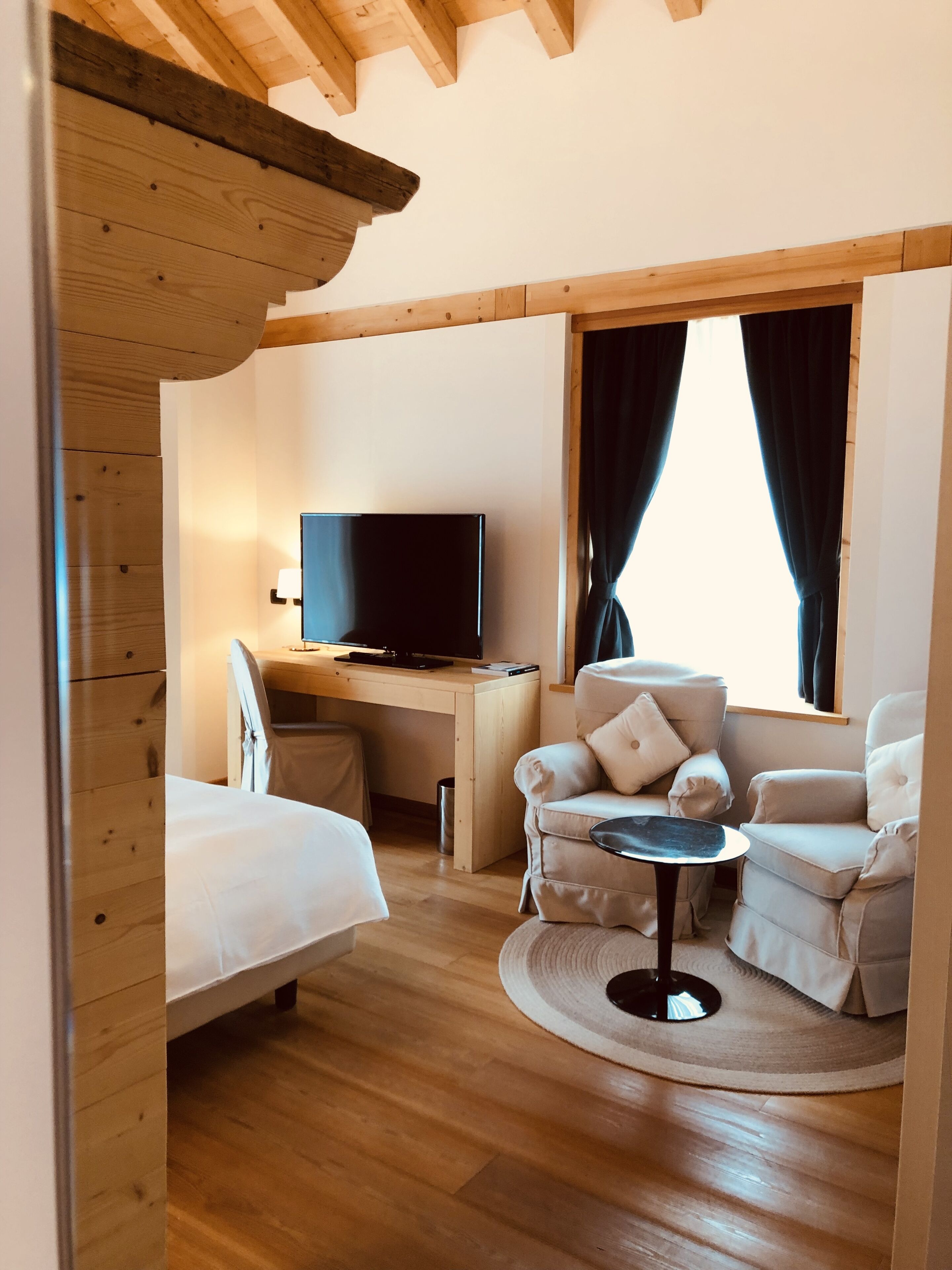 Ein gemütliches Zimmer mit einem Bett, einem Schreibtisch mit Fernseher, einem Sessel und einem kleinen Tisch.