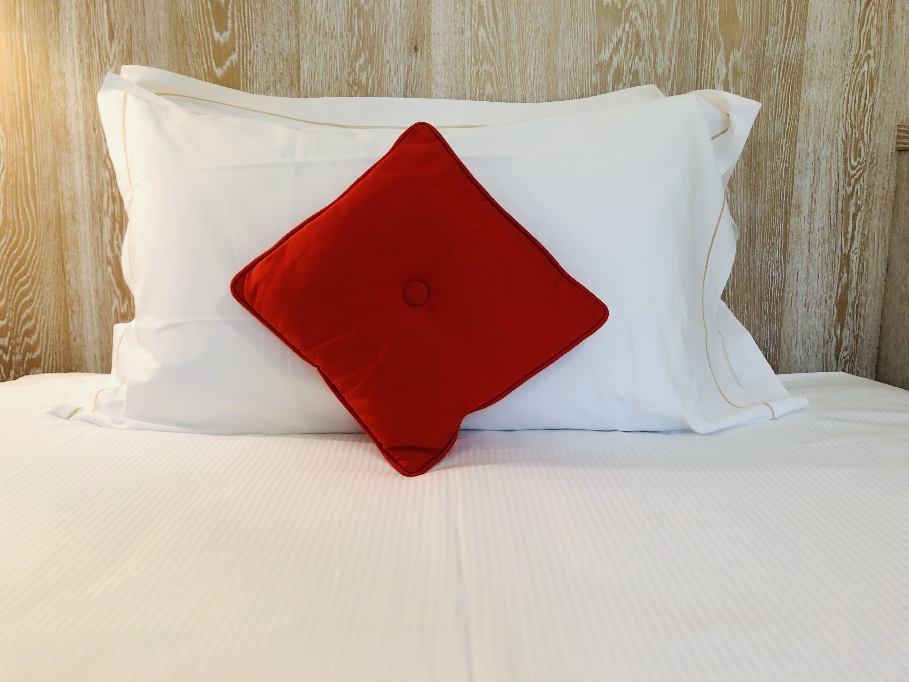 Una cama con ropa de cama blanca y una almohada roja.