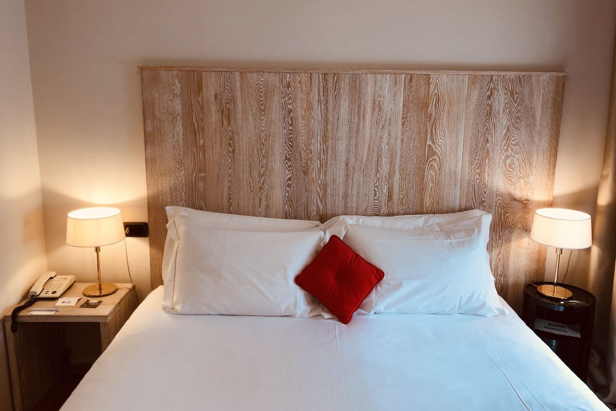 Habitación de hotel con una cama grande, dos lámparas de noche, un teléfono y una mesita con lámpara.