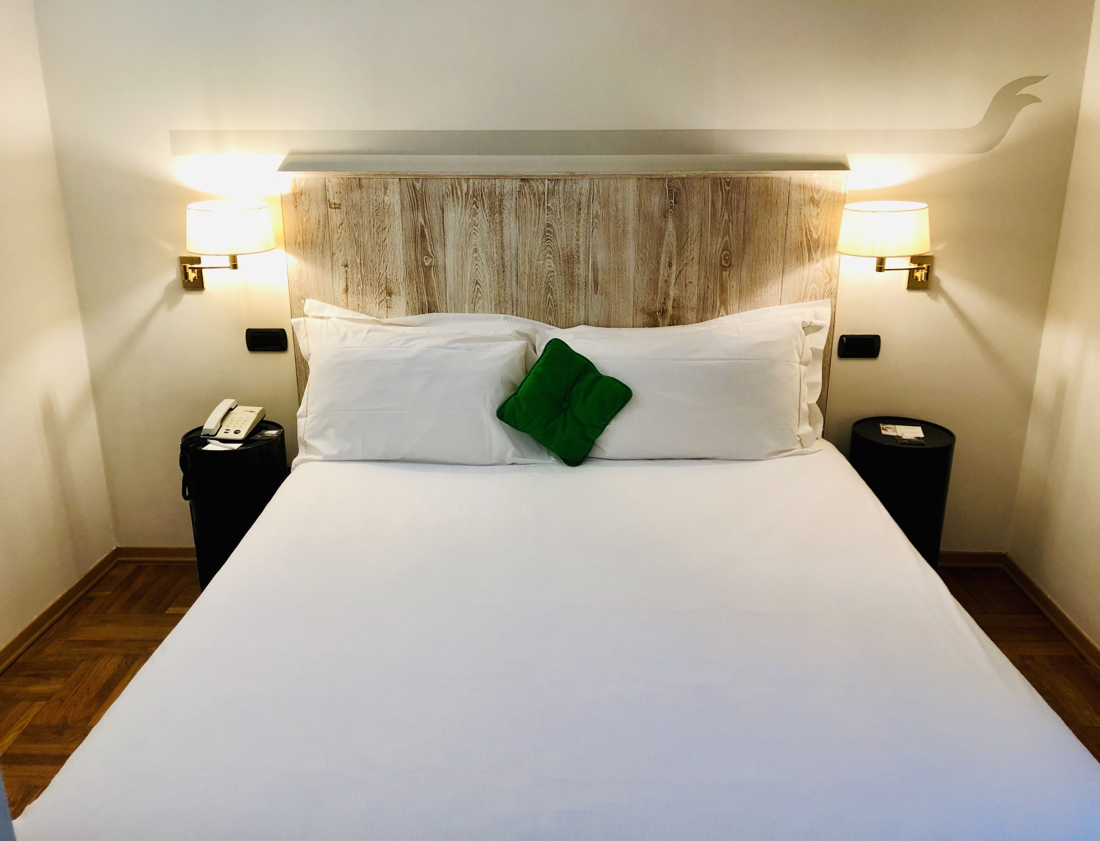 A hotel room with a large bed, two bedside lamps, a telephone, and a trash bin.