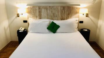 A hotel room with a large bed, two bedside lamps, a telephone, and a trash bin.