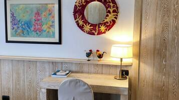 Una scrivania in legno con una sedia, un quadro incorniciato, uno specchio decorativo e una lampada.