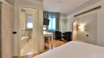 Habitación de hotel con cama, escritorio, silla, televisor y baño visible a través de una puerta abierta.