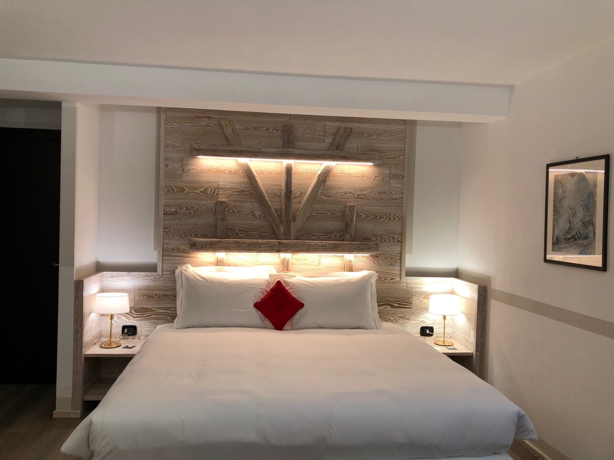 Une chambre d’hôtel avec un grand lit, deux tables de chevet avec des lampes, une tête de lit en bois et un tableau encadré au mur.