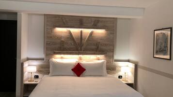 Une chambre d’hôtel avec un grand lit, deux tables de chevet avec des lampes, une tête de lit en bois et un tableau encadré au mur.