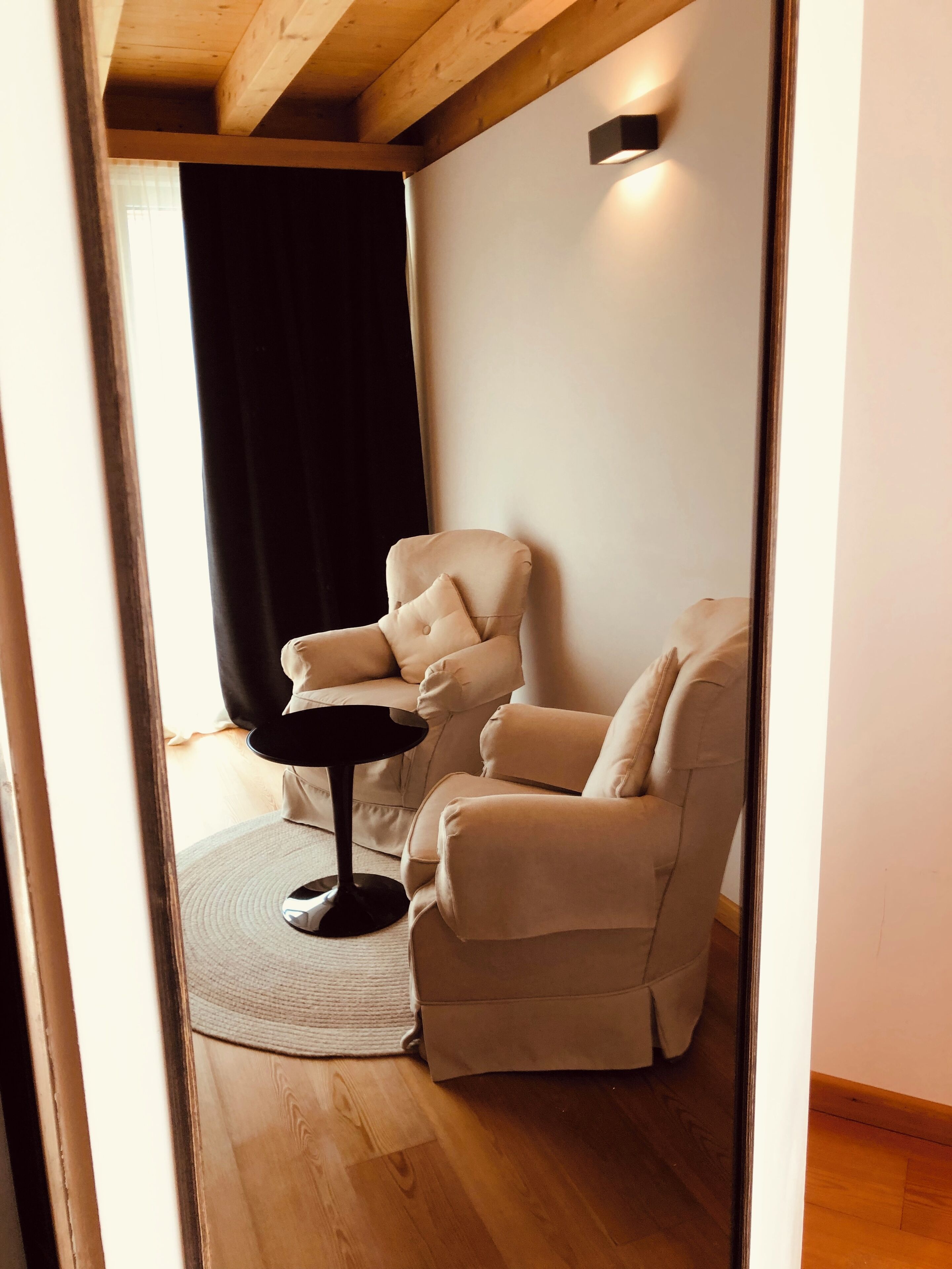 Ein Zimmer mit einem beigen Sofa, einem kleinen runden Tisch und einem dunklen Vorhang.