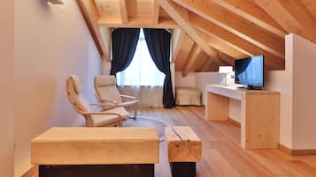 Um quarto de sótão aconchegante com vigas de madeira, uma cama, uma escrivaninha com televisão e duas cadeiras.