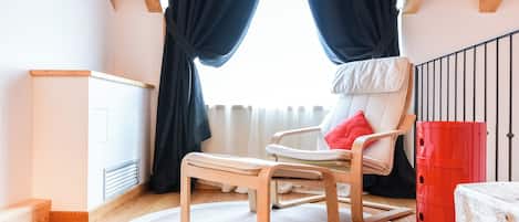 Una habitación con techo de madera, una silla blanca con cojín rojo, una mesa de madera y un barril rojo.