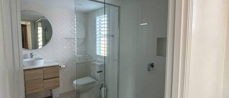Ein modernes Badezimmer mit Duschkabine aus Glas, einem weißen Waschbecken und einer Toilette.