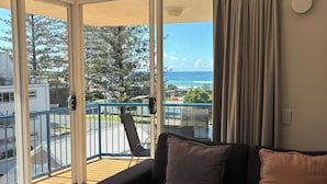 A living room with a black sofa, a round wooden coffee table, and a view of the ocean through large sliding glass doors. - San Mateo on Broadbeach (Broadbeach)