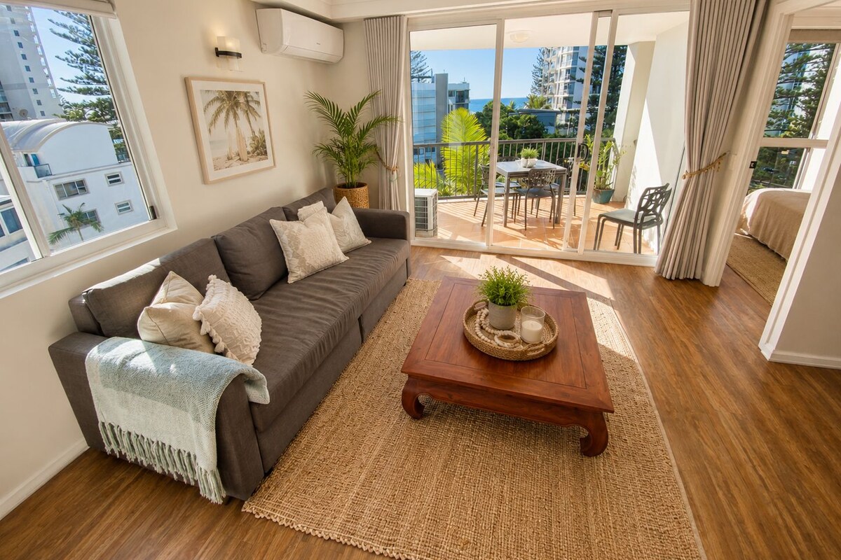 Una sala moderna con sofá, una mesa de centro y vistas a un balcón con mobiliario exterior.