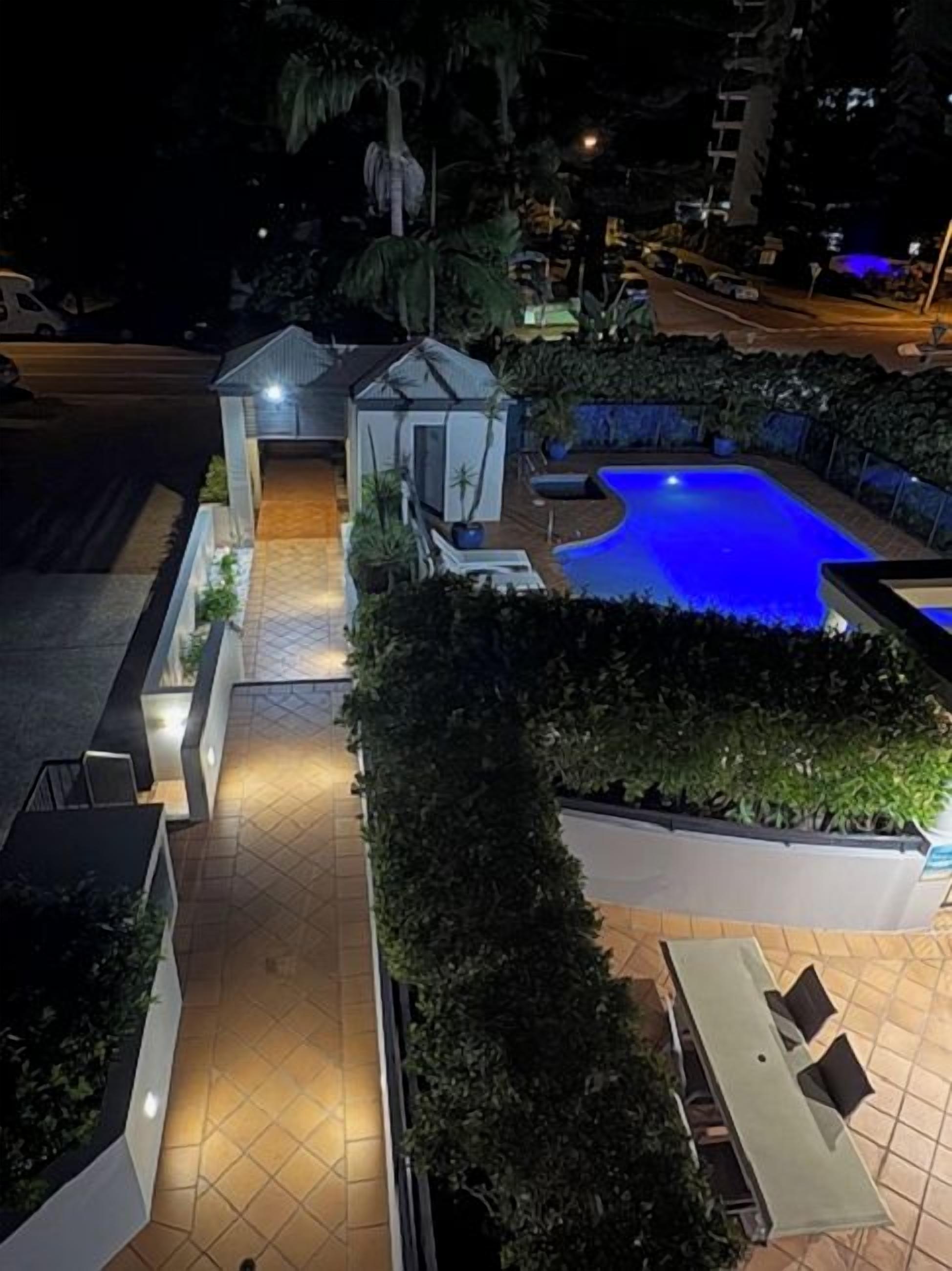 A nighttime view of a hotel courtyard with a swimming pool, a small gazebo, and a paved walkway.