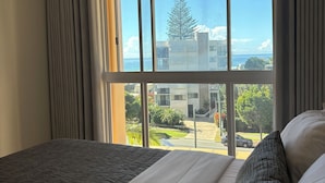 A hotel room with a large window, a bed with white and grey bedding, and a view of a building and greenery outside. - San Mateo on Broadbeach (Broadbeach)
