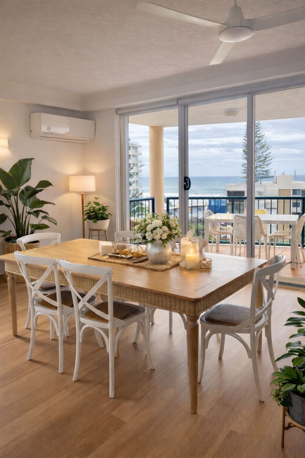 Un comedor con una mesa de madera, sillas blancas y vista al océano.