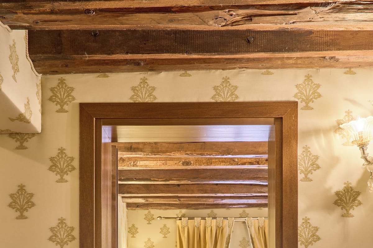 A room with a wooden ceiling, a bed with a white bedspread, a bedside table, and a chair.