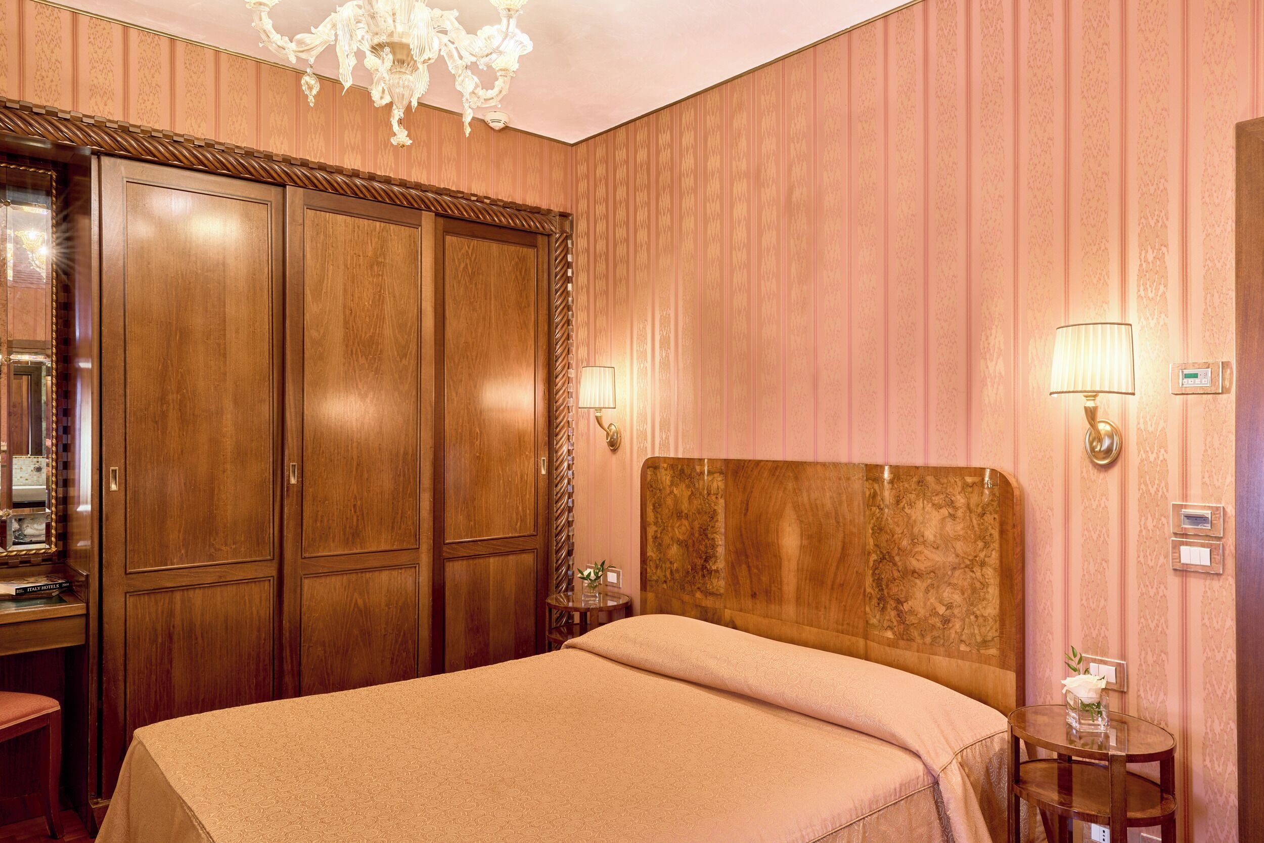 Habitación de hotel con una cama grande, armario de madera, un escritorio con espejo y un candelabro.