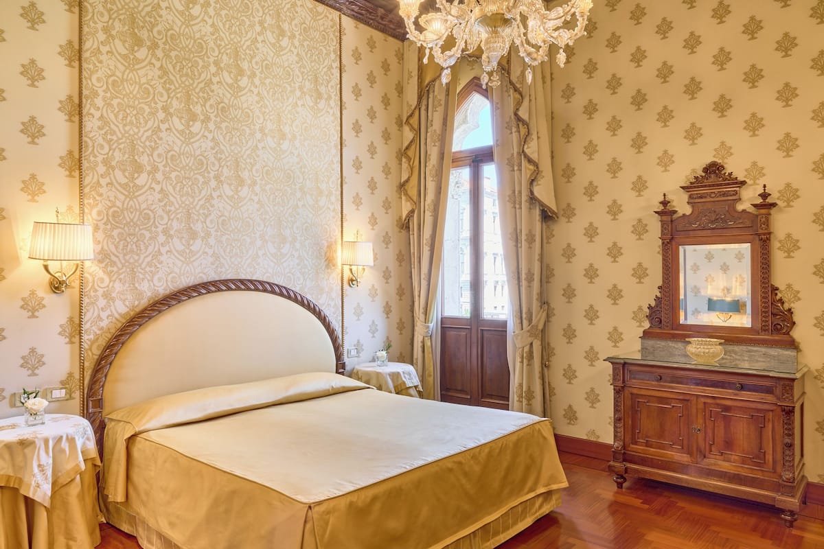 A bedroom with a large bed, two bedside tables with lamps, a wooden dresser, and a mirror.