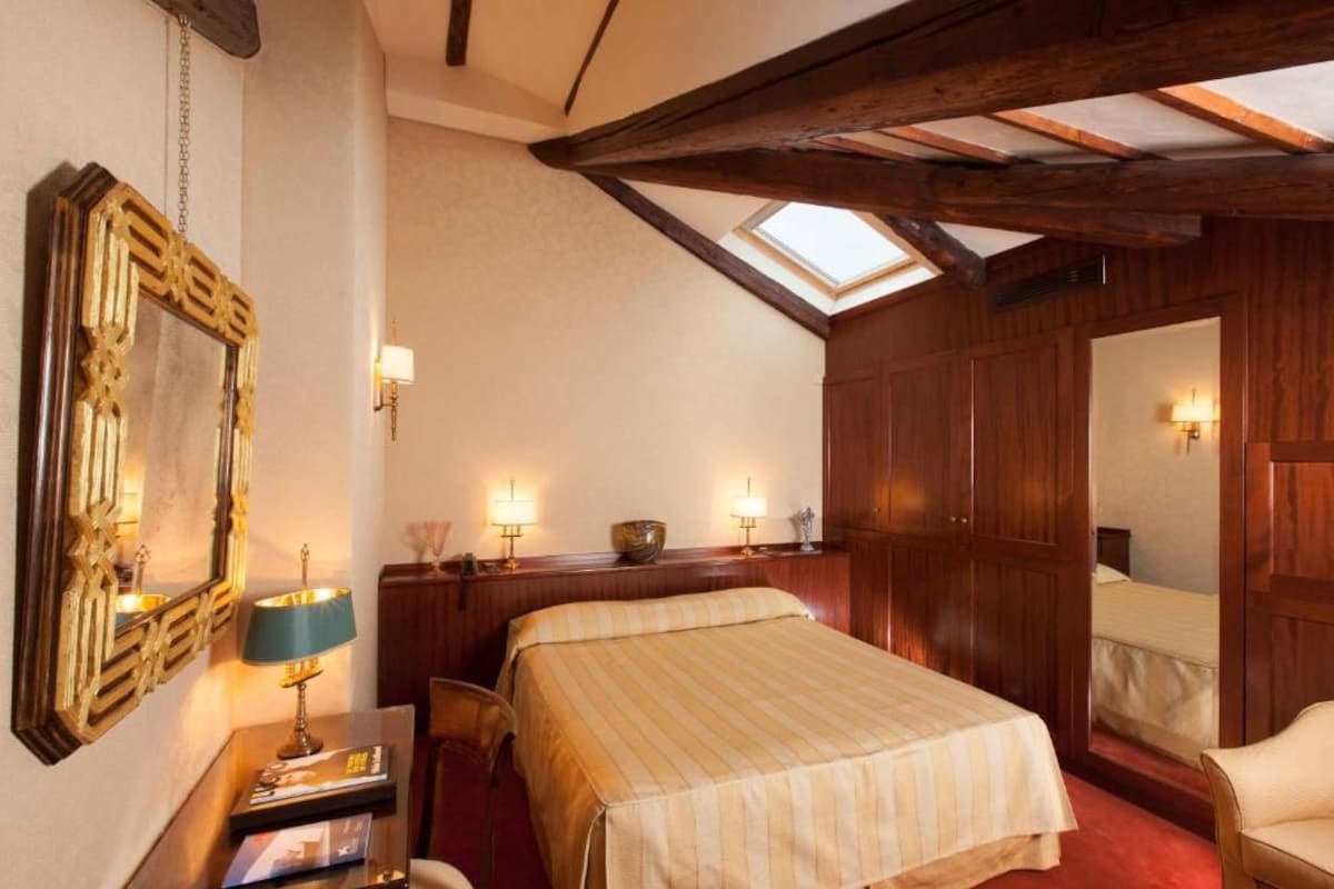 A hotel room with a bed, bedside tables, lamps, a mirror, and a skylight.