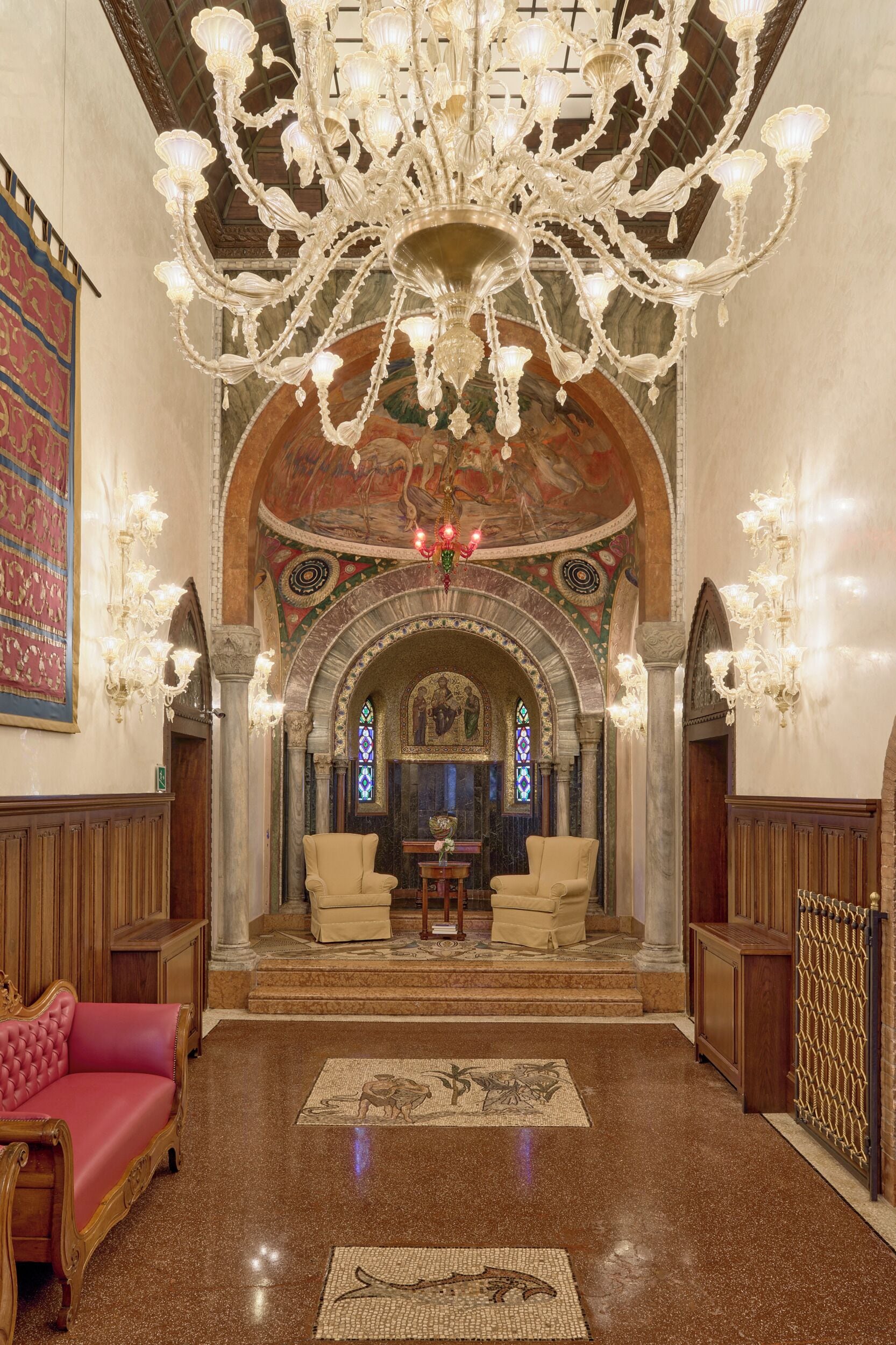 Um interior ornamentado com um candelabro, uma janela de vitrais e um soalho estampado.