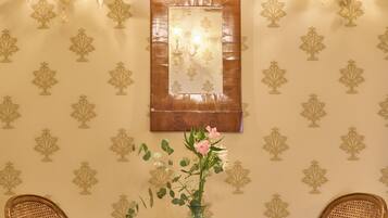 A room with two wicker chairs, a round wooden table with a vase, and wall-mounted lights.