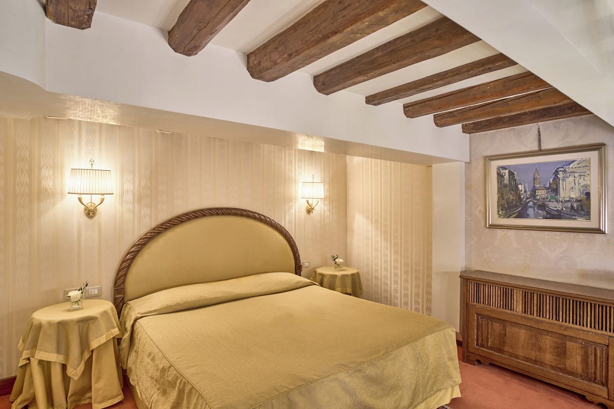 A hotel room with a large bed, two bedside tables, a nightstand, a wooden bench, and a painting on the wall.