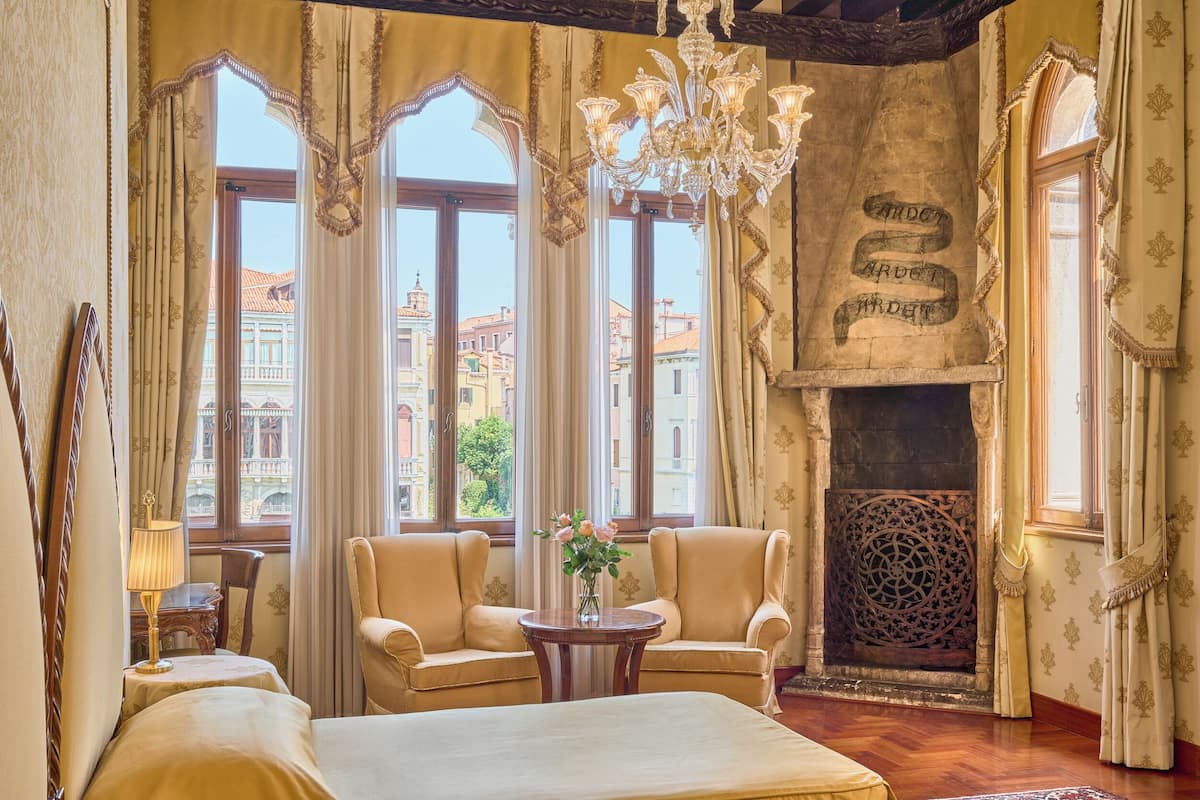 A room with two armchairs, a bed, a chandelier, and a fireplace with a decorative screen.