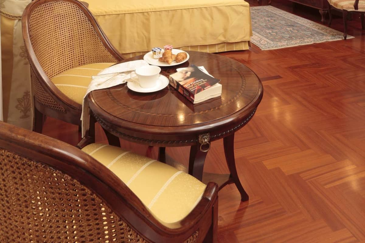 A hotel room with a bed, a wooden chair, a small round table with a book and a cup, and a television on a wooden cabinet.