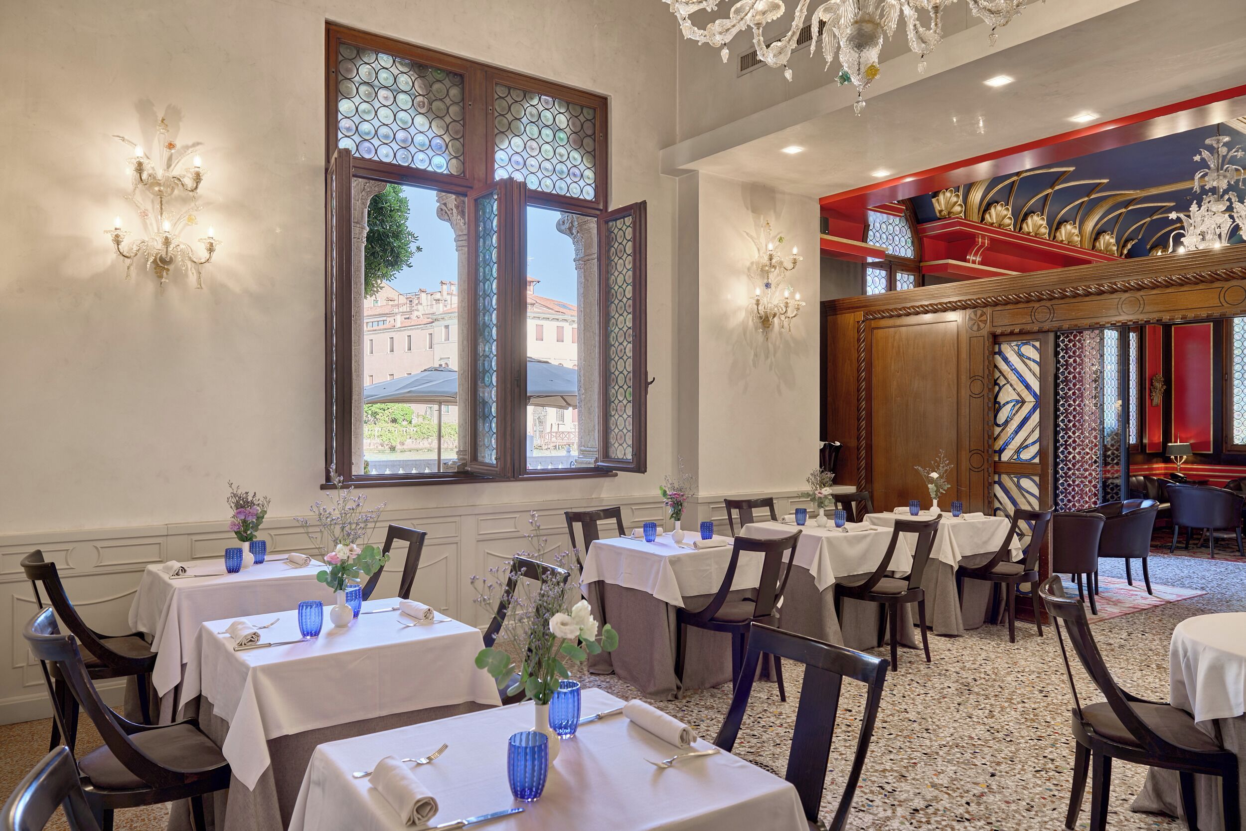 Ein Hotelrestaurant mit gedeckten Tischen, großen Fenstern mit Verzierglas und einer Kristallleuchter.