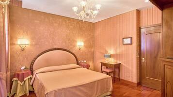 Un dormitorio con una cama grande, dos lámparas de noche, un candelabro, una puerta de madera y una mesita con una lámpara.