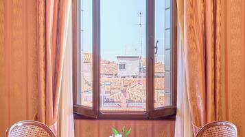 Una habitación con ventana, dos sillas de mimbre, una mesita redonda con un florero y paredes de madera.