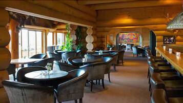 A cozy log cabin-style restaurant with round tables and chairs, a bar area, and a mural on the wall.