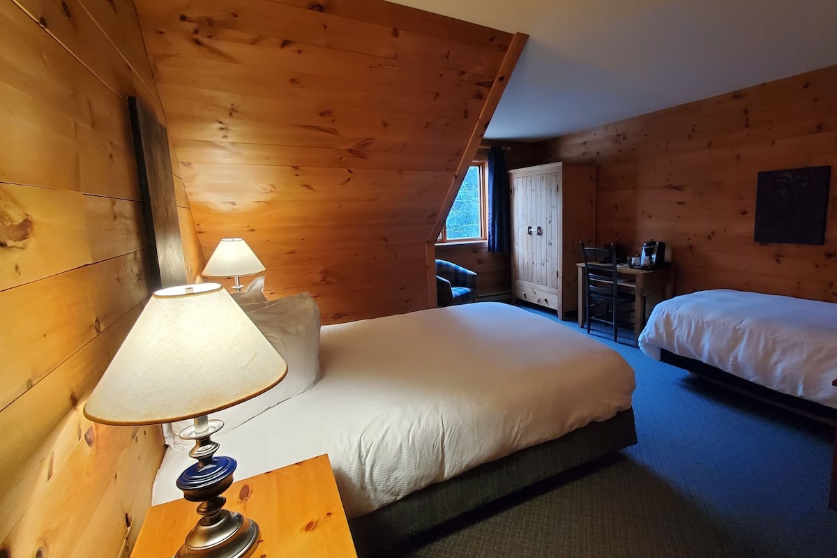 Ein Holzhüttenraum mit zwei Betten, einem Schreibtisch und einer Lampe.