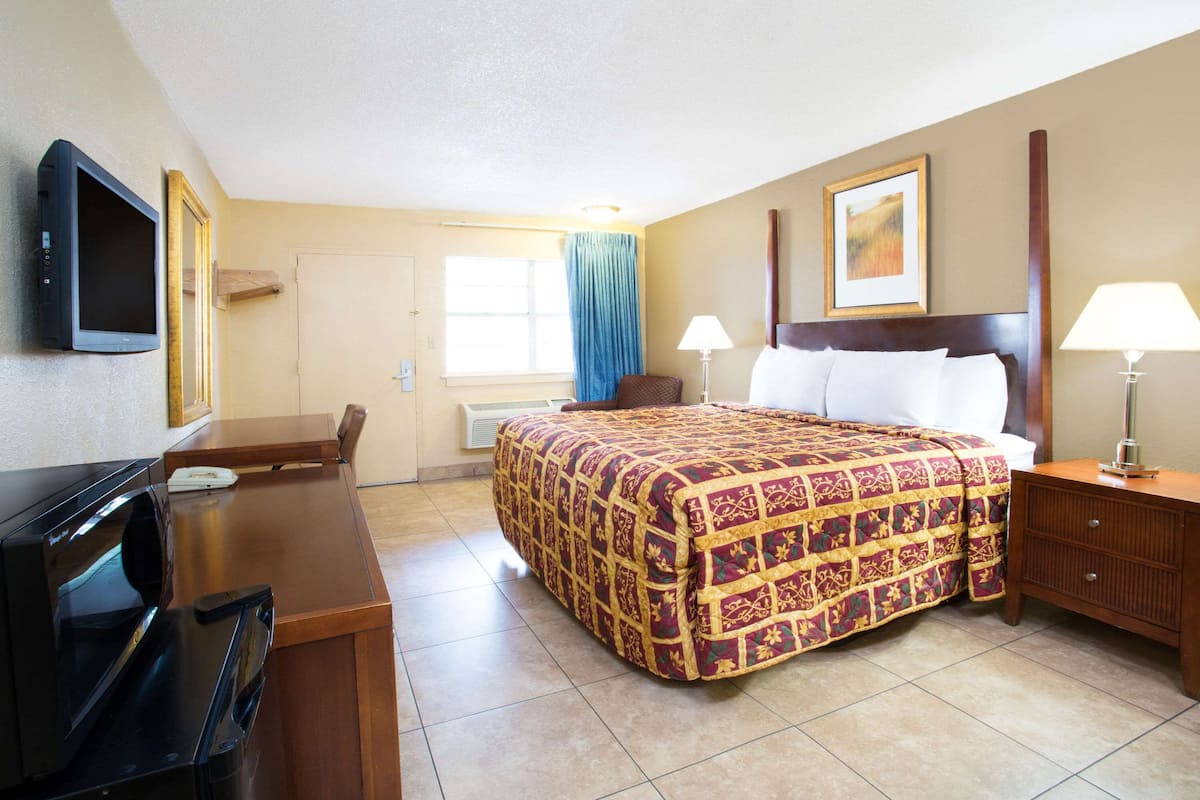A hotel room with a bed, a desk, a television, and a window with curtains.