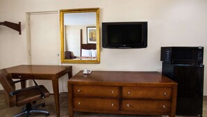 Habitació d'hotel amb escriptori de fusta, una cadira, un armari, televisió i nevera.