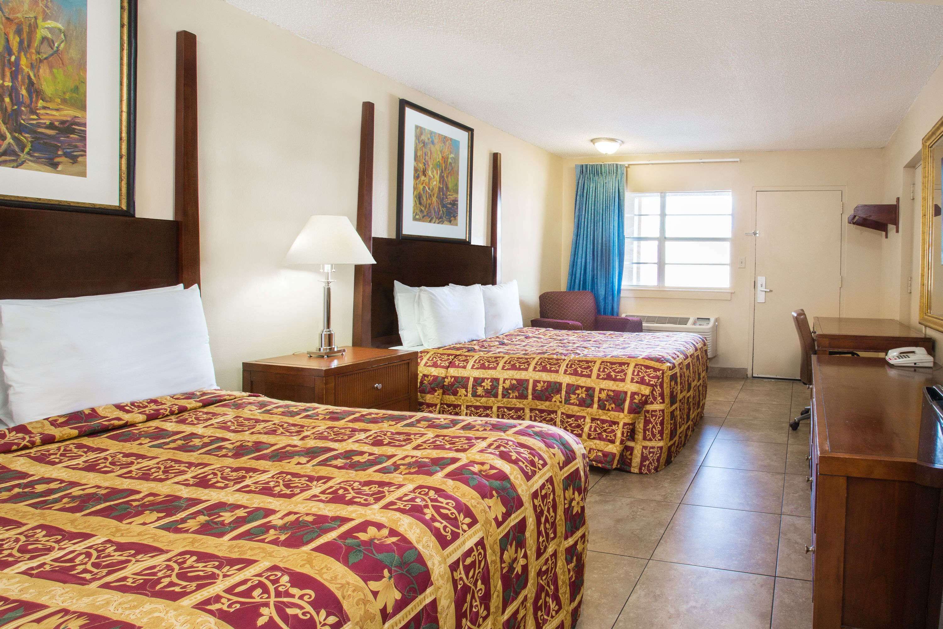 A hotel room with two beds, a desk, a chair, a lamp, and a window with curtains.