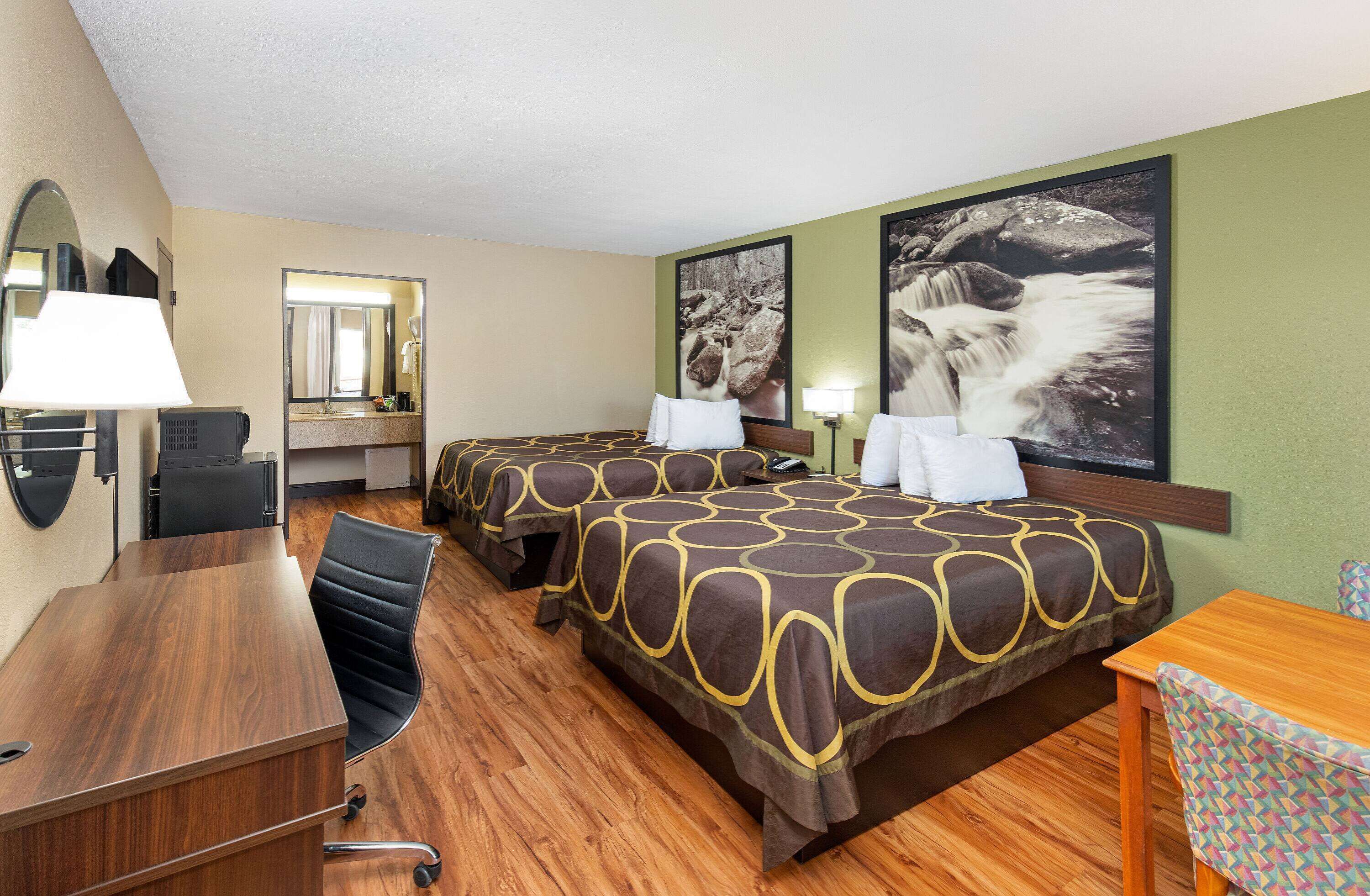 A hotel room with two beds, a desk, a chair, a mirror, and artwork on the walls.