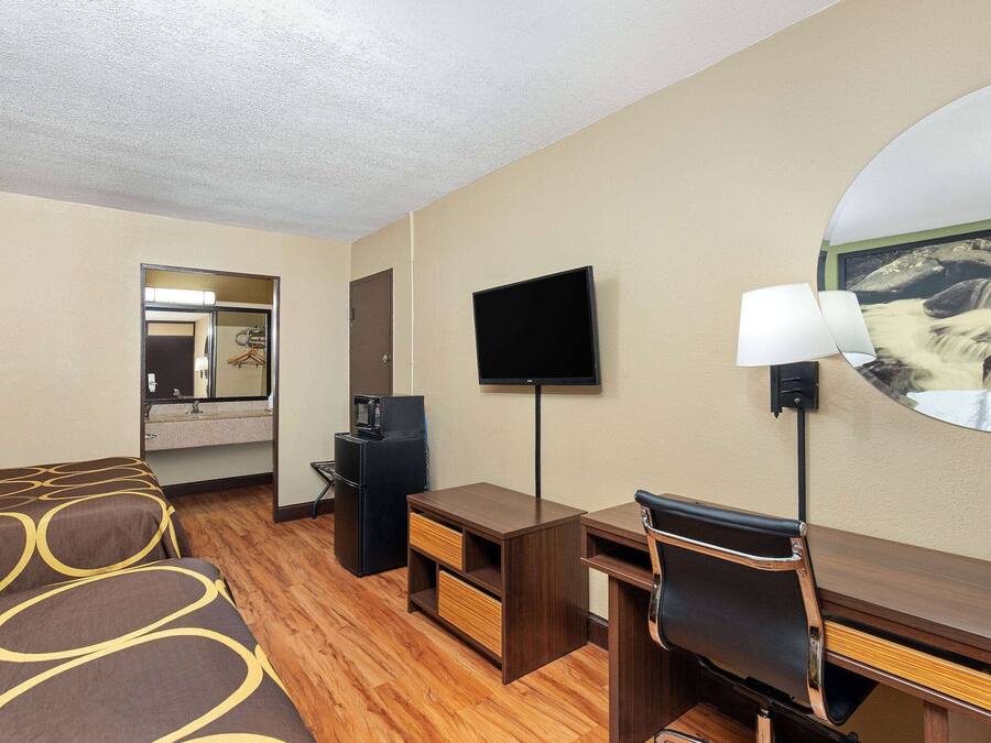 A hotel room with a bed, a desk, a chair, a television, a mirror, and a picture of a waterfall on the wall.